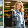 A blonde woman holds a black reusable insulated cooler bag in front of a grocery store aisle.