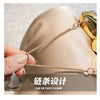 A close-up of a gold chain strap accessory being held against a beige fabric, showcasing the details of the design.