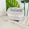 A light gray fabric storage basket with white lace trim and a heart pattern sits on a book.