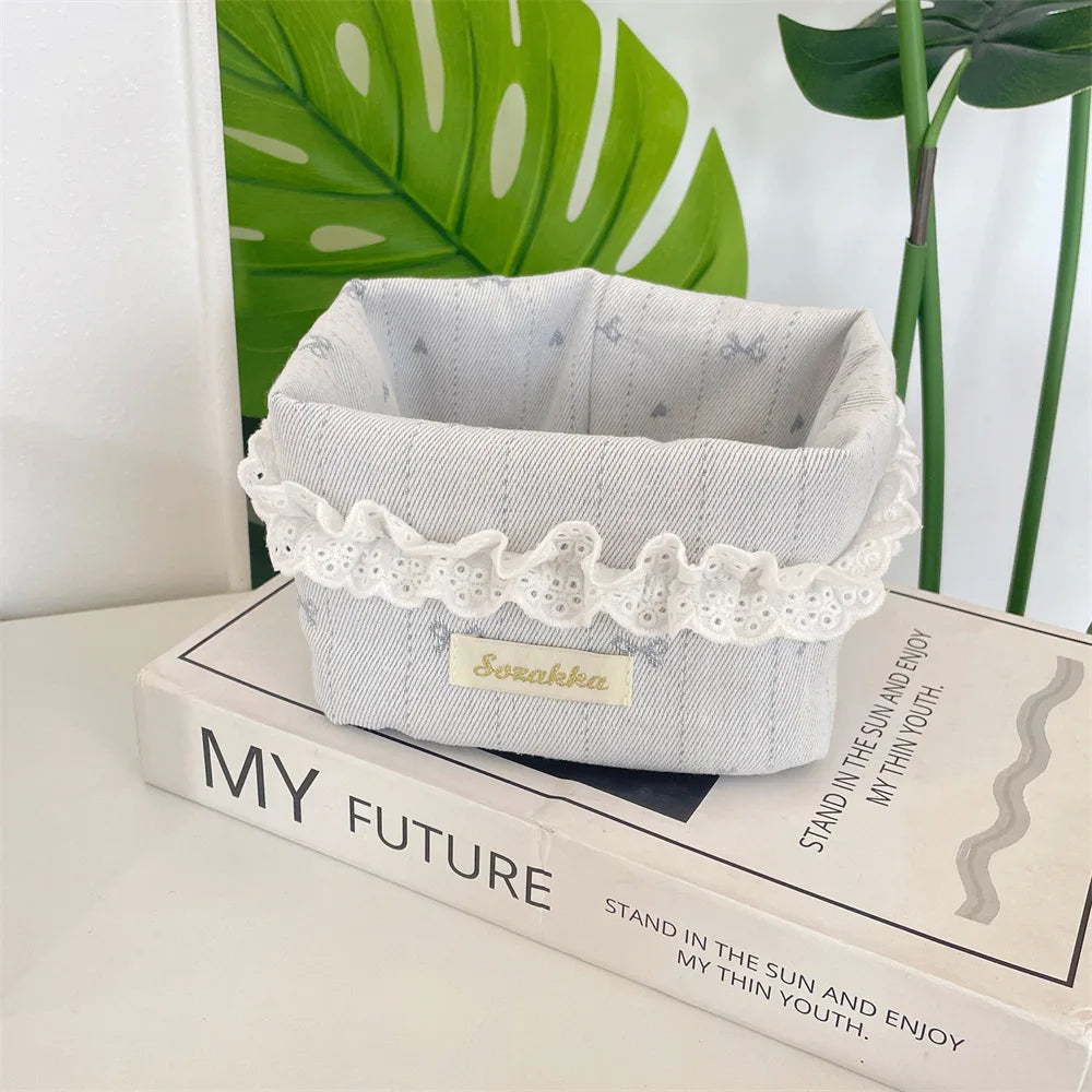 A light gray fabric storage basket with white lace trim and a heart pattern sits on a book.