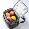 A silver insulated thermal lunch bag is open, revealing three fresh apples and a yellow lemon inside.