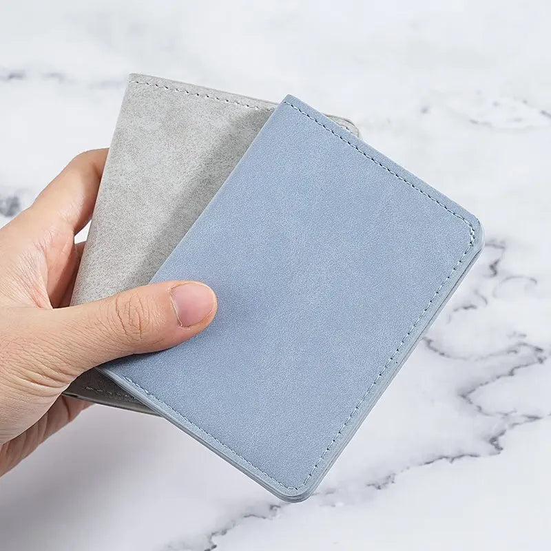 A hand holds a light blue ultra-thin multi-slot card wallet next to a gray one on a white marble surface.