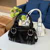 A black PU leather shoulder bag with silver rivets and a white strap resting on a white table.