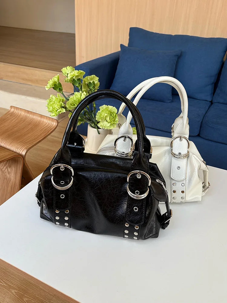 A black PU leather shoulder bag with silver rivets and a white strap resting on a white table.