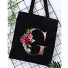 Black canvas tote bag featuring a large gold letter G with floral accents