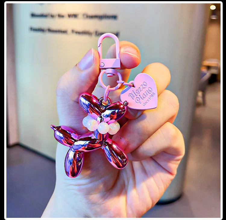 A hand holds a pink balloon dog keychain charm with a padlock and a heart-shaped tag.