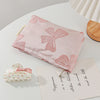 A pink cosmetic organizer bag with a bow knot design rests on a white surface next to a small floral item.