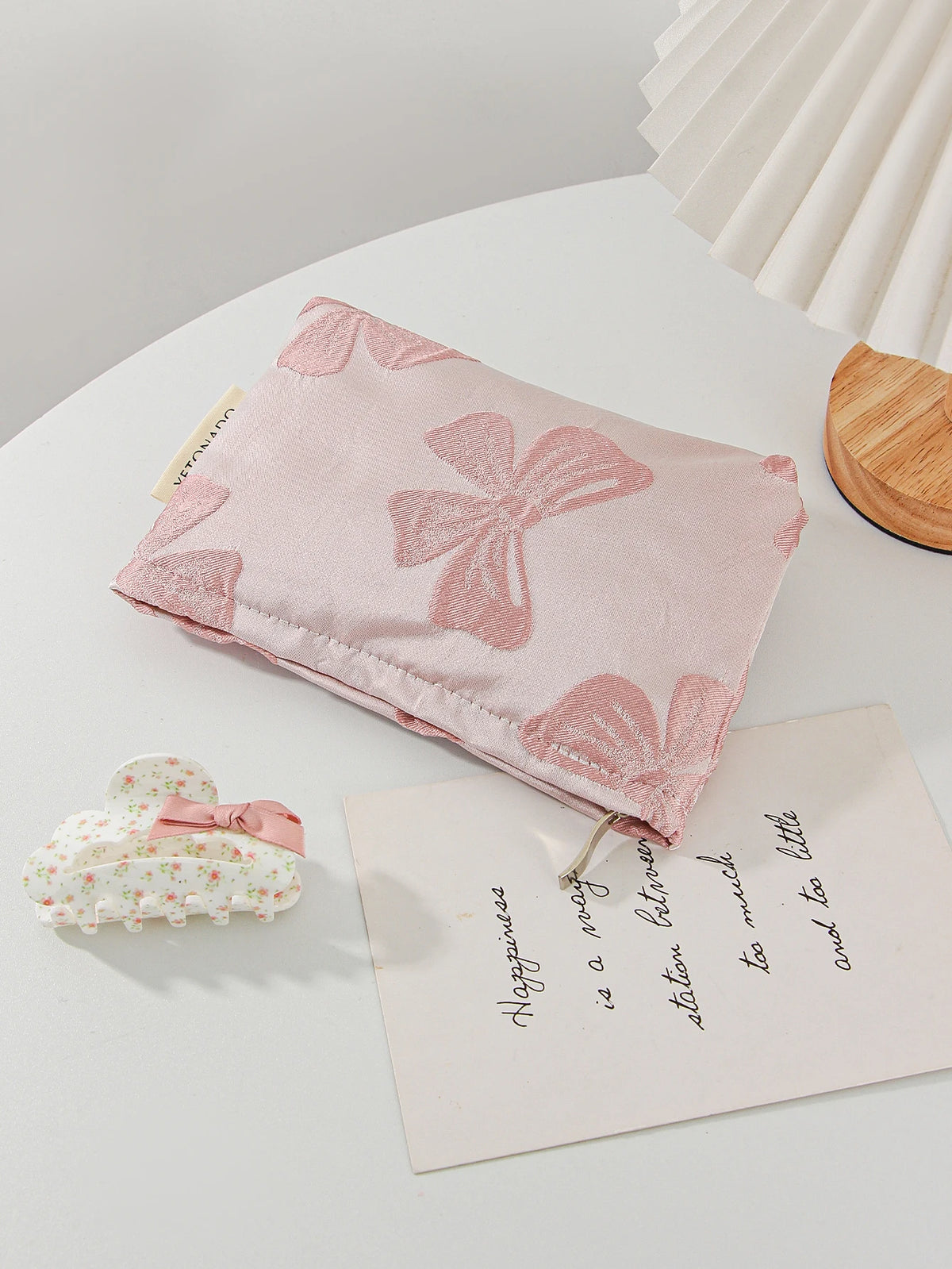 A pink cosmetic organizer bag with a bow knot design rests on a white surface next to a small floral item.