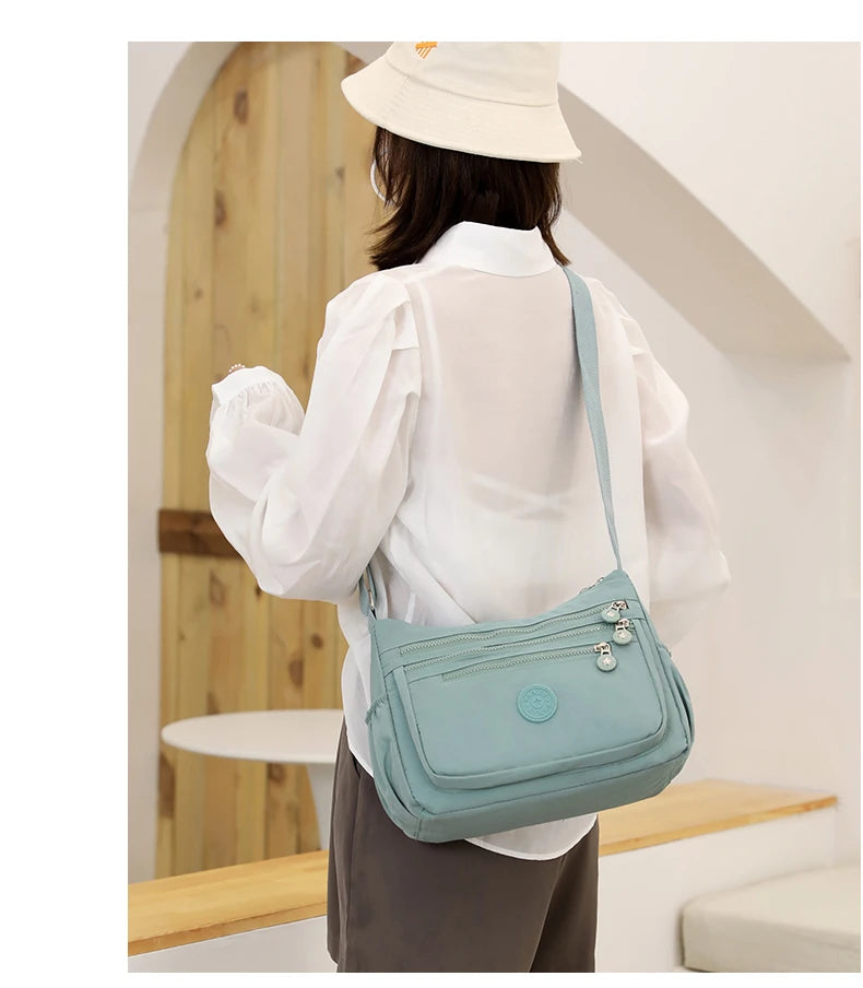 A woman wearing a white shirt and straw hat is shown from the back carrying a light blue waterproof nylon crossbody shoulder 
