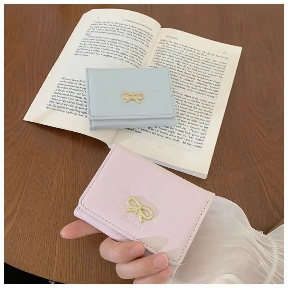 Cartera de cuero sintético rosa tríptico con detalle de lazo dorado sobre un cuaderno abierto.