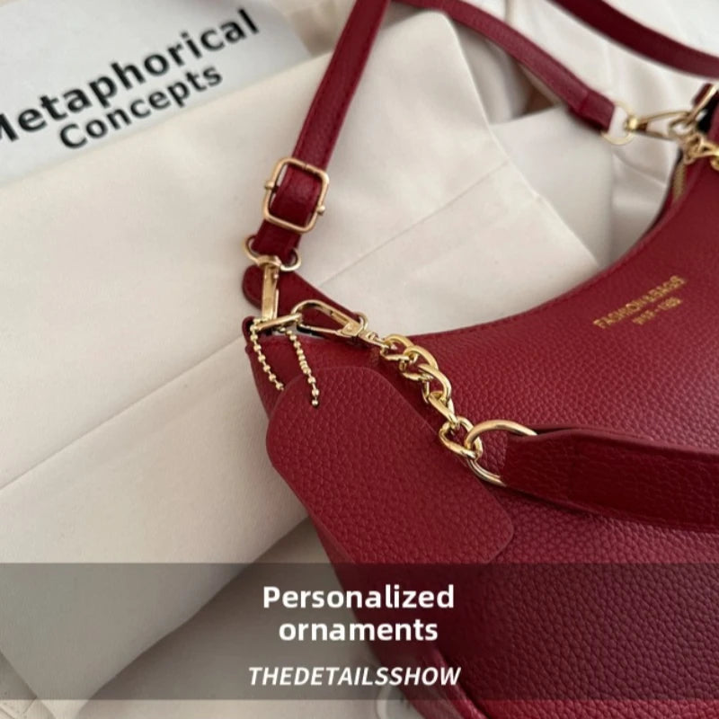 A close-up of a maroon leather shoulder bag with gold hardware and a small cherry pendant resting on white fabric.