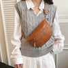 A woman wearing a gray knitted vest over a white shirt and a brown leather crossbody bag.