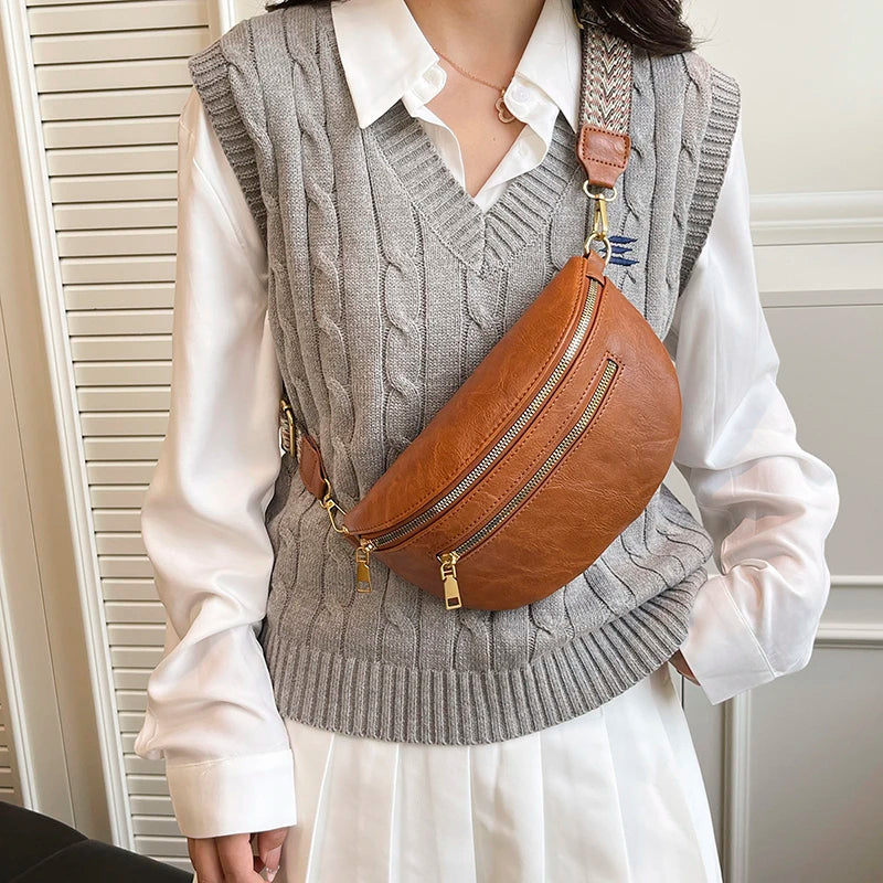 A woman wearing a gray knitted vest over a white shirt and a brown leather crossbody bag.