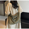 Une femme tient un manteau beige clair et porte un sac à main en velours rayé vert olive texturé.