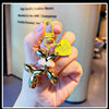 A hand holds a gold-colored balloon dog keychain charm with a yellow clasp and a yellow tag.