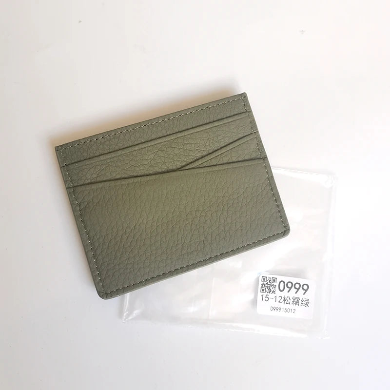 Porte-cartes en cuir véritable vert olive plié dans une gaine en plastique transparent.