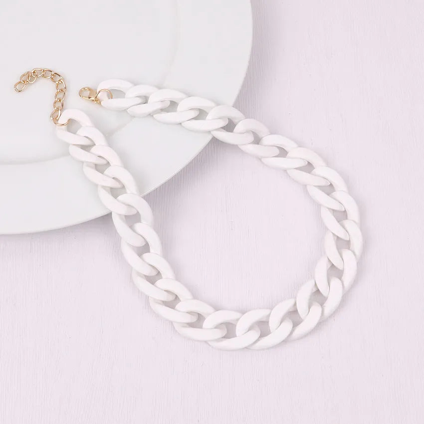 A white acrylic statement choker necklace with a gold-colored clasp is displayed on a white background.