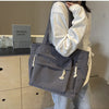 A person holds a gray corduroy shoulder bag with zipper details in a light-colored sweater.