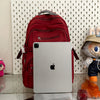 A white laptop is placed in front of a red backpack, with a plush toy visible on the right.