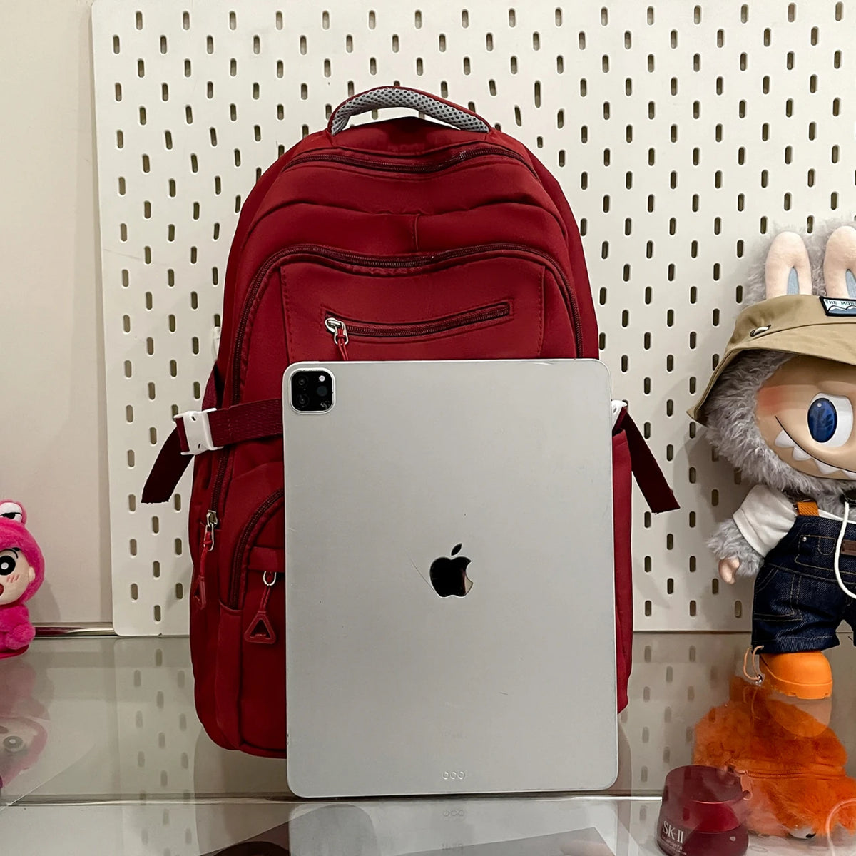 A white laptop is placed in front of a red backpack, with a plush toy visible on the right.