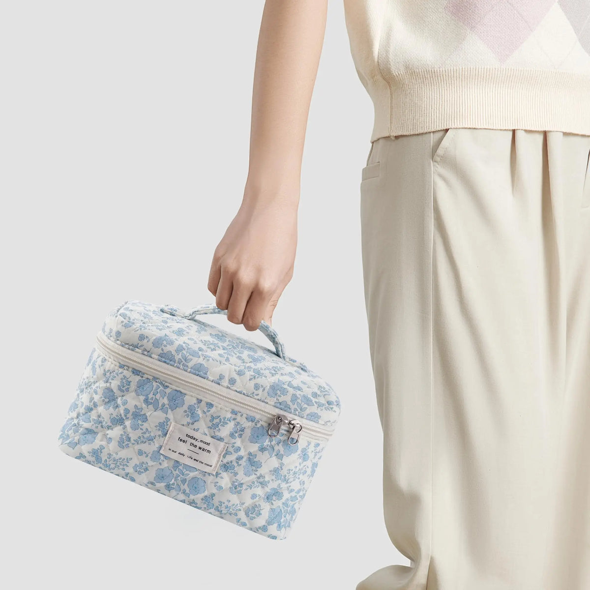 A light blue quilted cotton makeup organizer set being held by a person next to beige pants.