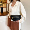A woman holds a black PU leather crossbody bag with a gold chain strap against a white shirt.