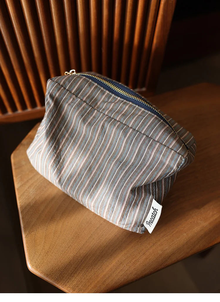 Pochette de rangement cosmétique à rayures gris et beige sur une surface en bois.