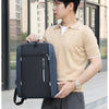 A young man wearing a beige polo shirt and dark pants holds a black nylon travel backpack.