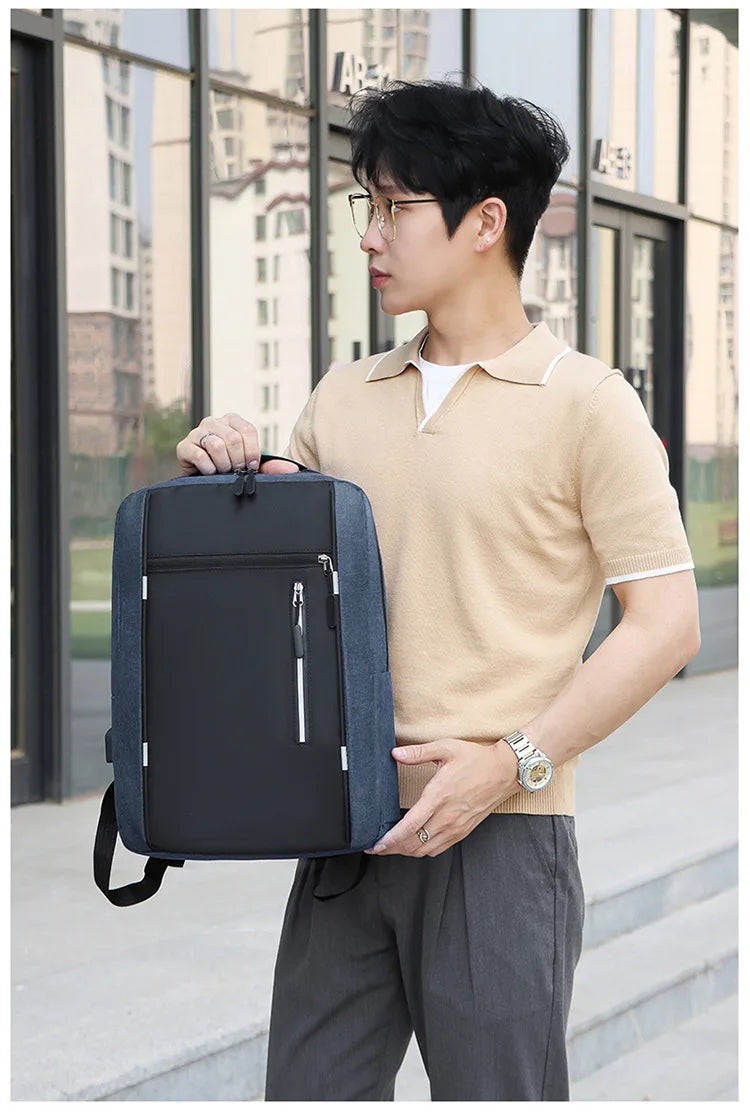 A young man wearing a beige polo shirt and dark pants holds a black nylon travel backpack.