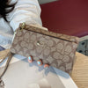A close-up of a taupe crocodile print zipper wallet with a gold accent, held by a person's hand.