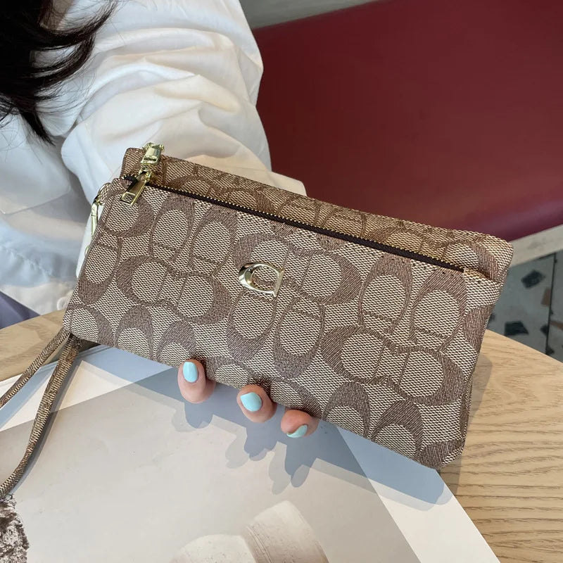 A close-up of a taupe crocodile print zipper wallet with a gold accent, held by a person's hand.