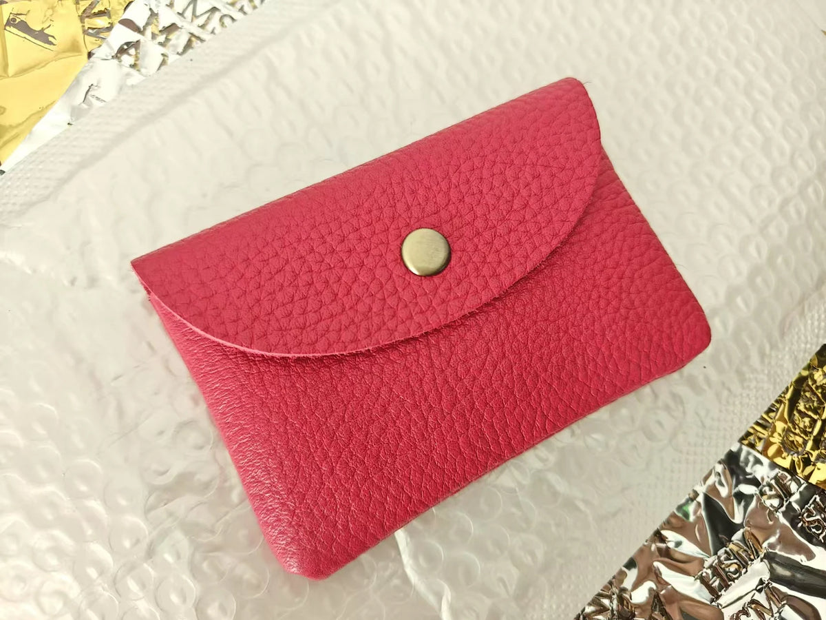 A vibrant pink genuine leather card holder with a gold-toned snap closure resting on a white textured surface.