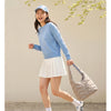 A young woman wearing a light blue sweater and a white skirt is walking outdoors while carrying a beige quilted nylon shoulde