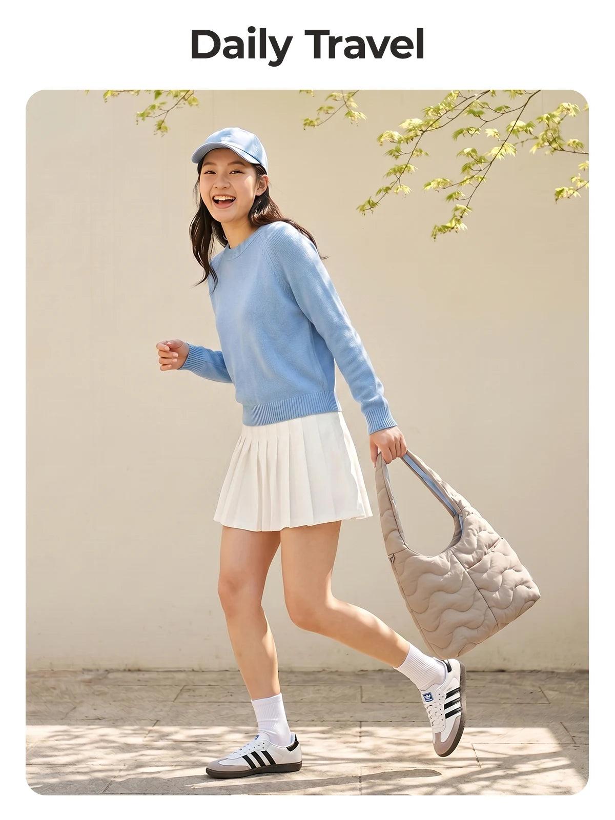 A young woman wearing a light blue sweater and a white skirt is walking outdoors while carrying a beige quilted nylon shoulde