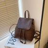 Petit sac à dos rétro marron avec cordon, posé sur une boîte blanche.