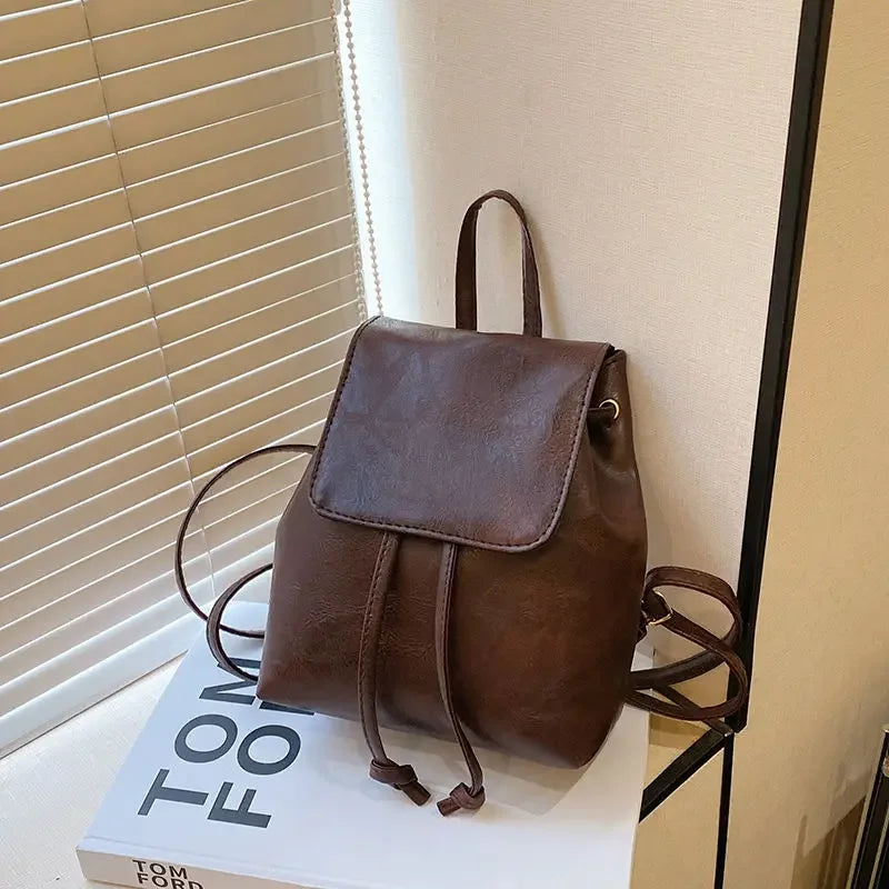 Petit sac à dos rétro marron avec cordon, posé sur une boîte blanche.