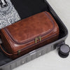 A brown leather toiletry bag with brass hardware is shown inside a gray case.