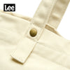 Close-up of a cream colored Korean style Oxford cloth tote bag featuring a stitched detail and brass button.