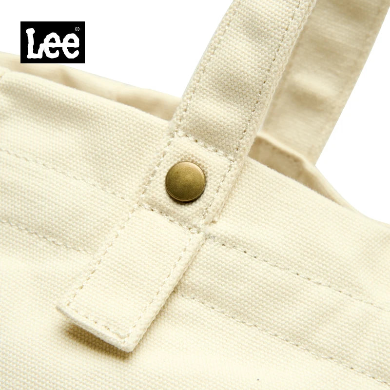 Close-up of a cream colored Korean style Oxford cloth tote bag featuring a stitched detail and brass button.