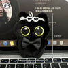 Colgante llavero de peluche de gato negro con ojos grandes y un lazo, apoyado en el teclado de una laptop.