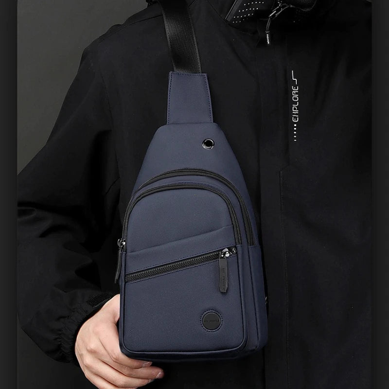 A navy blue lightweight nylon crossbody sling bag is shown being held against a black jacket.