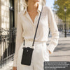 A woman wearing a white shirt and pants holds a black PU leather crossbody phone bag.