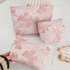 A hand holds a pink cosmetic organizer bag featuring a delicate bow knot pattern on a white surface.