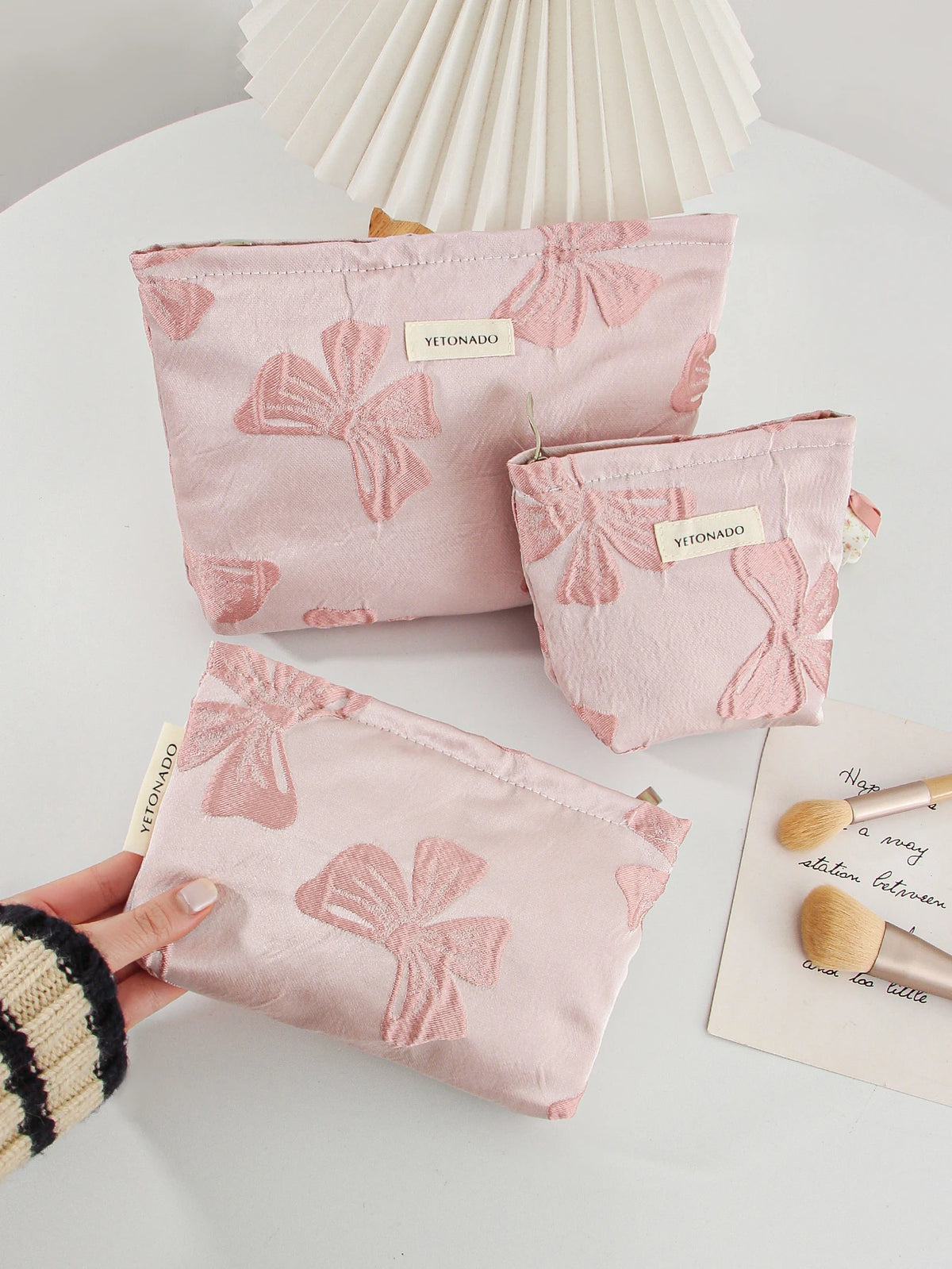A hand holds a pink cosmetic organizer bag featuring a delicate bow knot pattern on a white surface.
