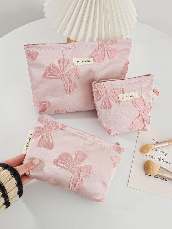 A hand holds a pink cosmetic organizer bag featuring a delicate bow knot pattern on a white surface.