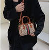 A woman holds an elegant brown leather tote diaper bag with a gold crossbody strap against a black coat.