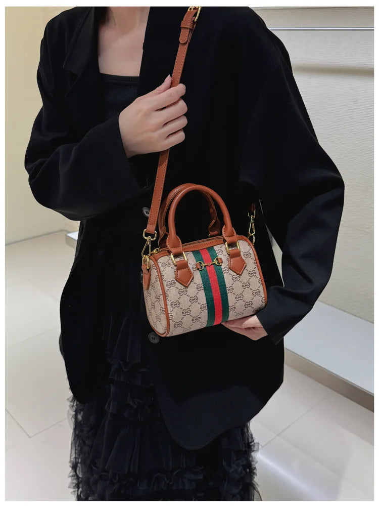 A woman holds an elegant brown leather tote diaper bag with a gold crossbody strap against a black coat.