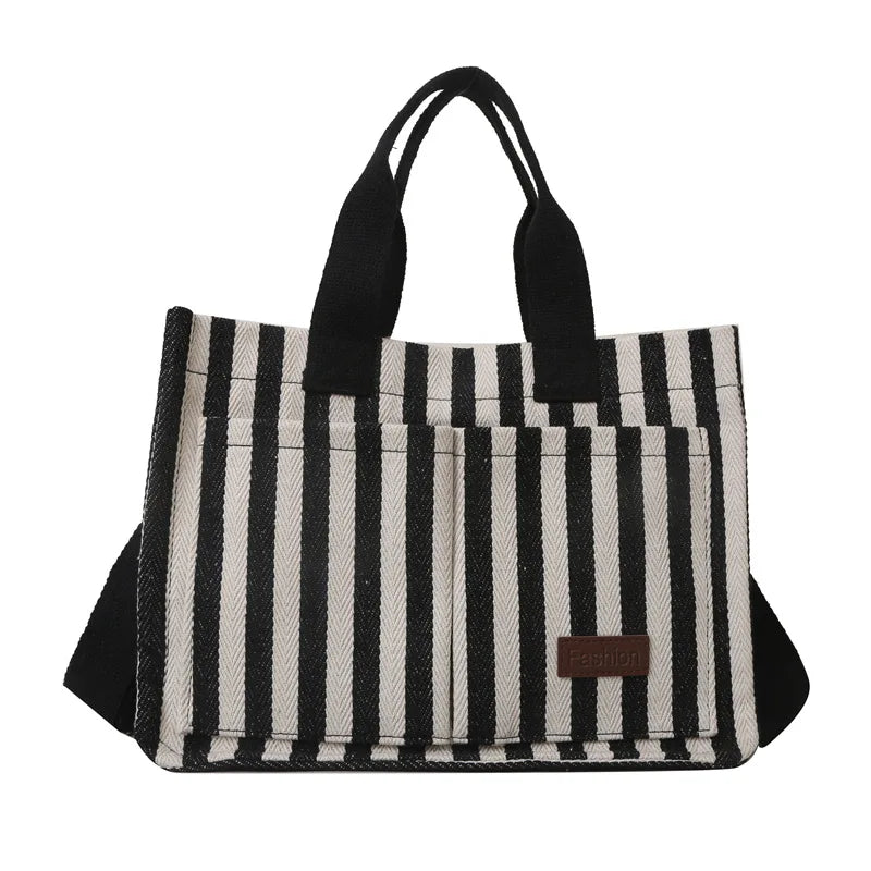 Sac bandoulière en toile à rayures noires et blanches avec poignées noires.