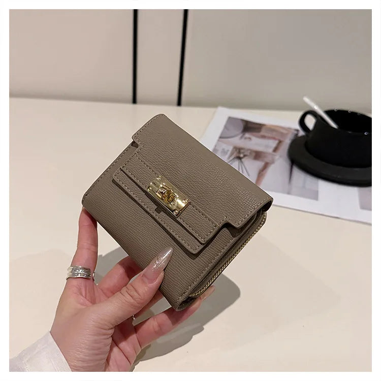 A hand holds a beige multi-slot card holder with gold accents on a white surface.