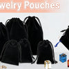 Colección de bolsitas de joyería de terciopelo negro y bolsas de regalo de papel grueso con asas de cuerda sobre fondo blanco